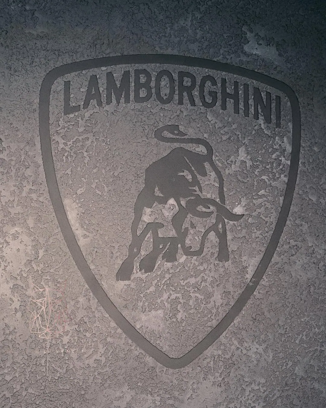 Grey textured wall with a Lamborghini shield logo