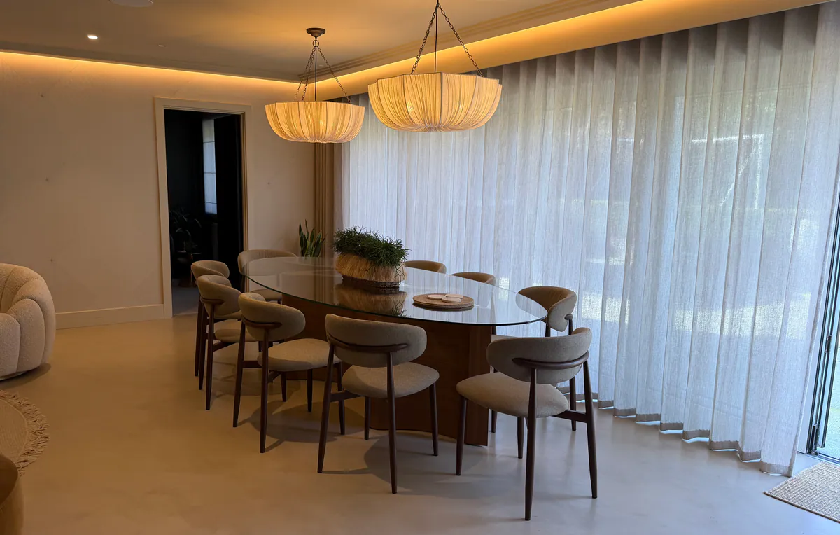Open-plan dining area with a pale microcement floor, an oval glass table, upholstered chairs and cove lighting