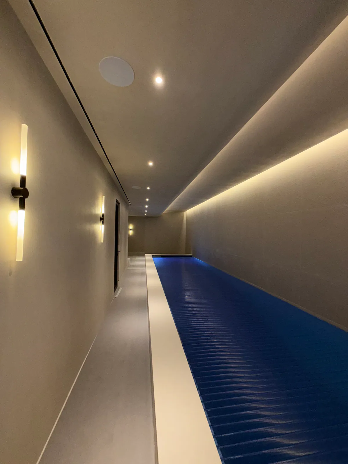 Narrow pool hall seen along a covered pool, with wall lights and a cove-lit ceiling