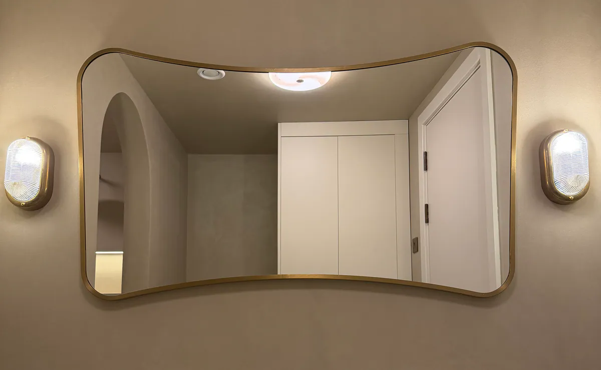 Brass-framed mirror between two brass wall lights on a warm taupe wall