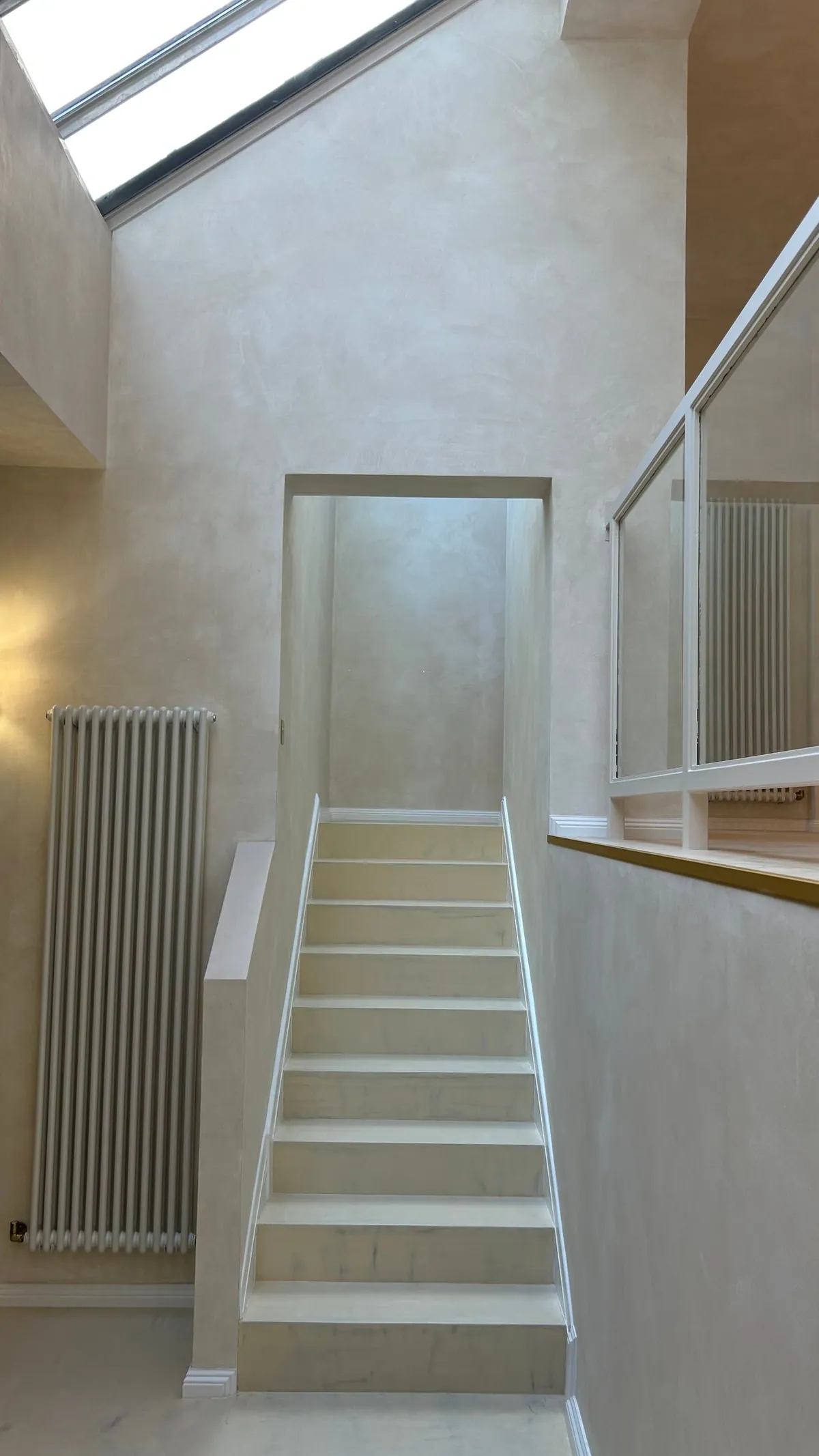 Pale staircase with a glass balustrade, a tall radiator and a skylight above