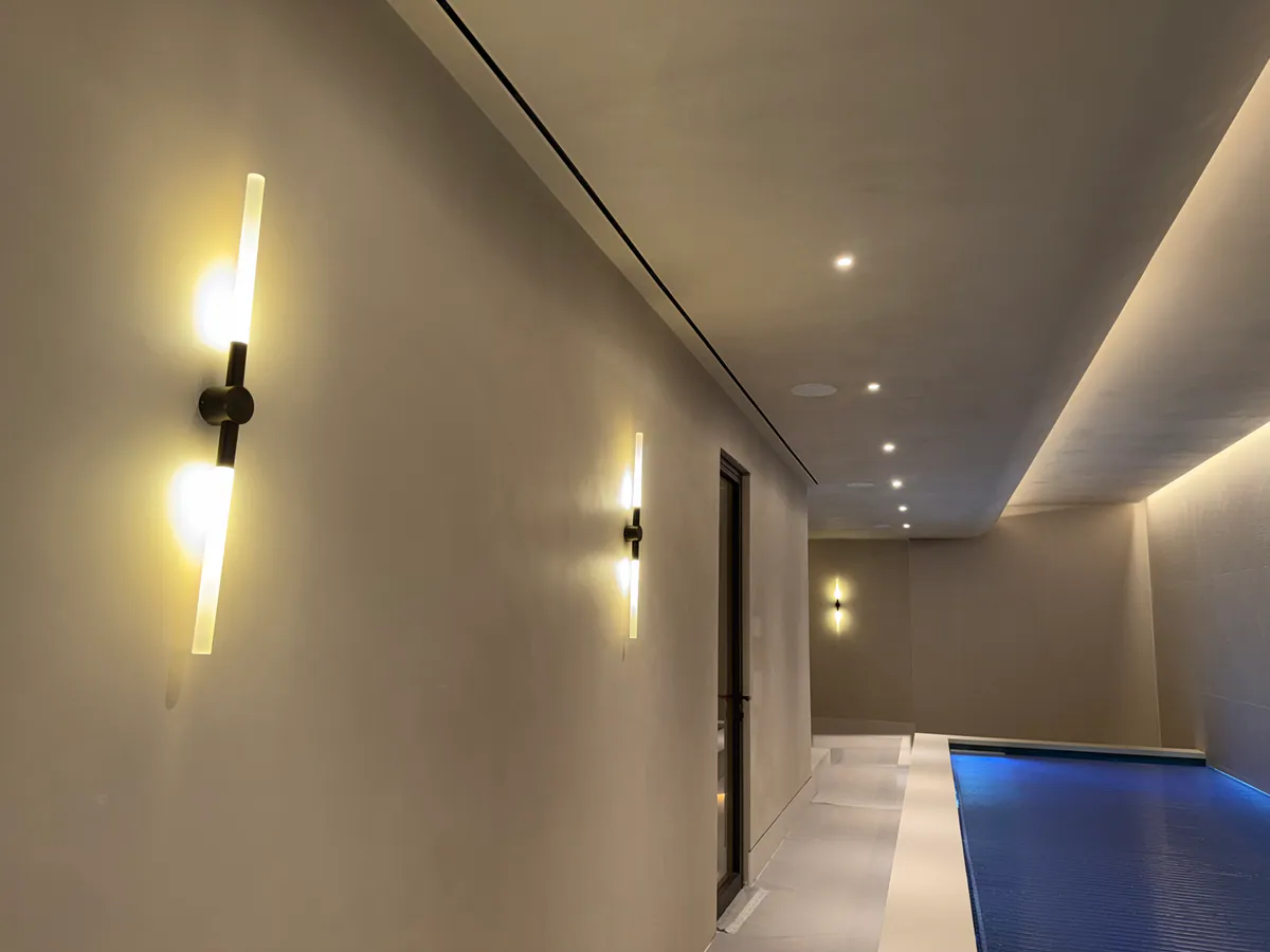 Wall lights on a pale pool hall wall, with a dark-framed door and a covered pool beside a pale surround