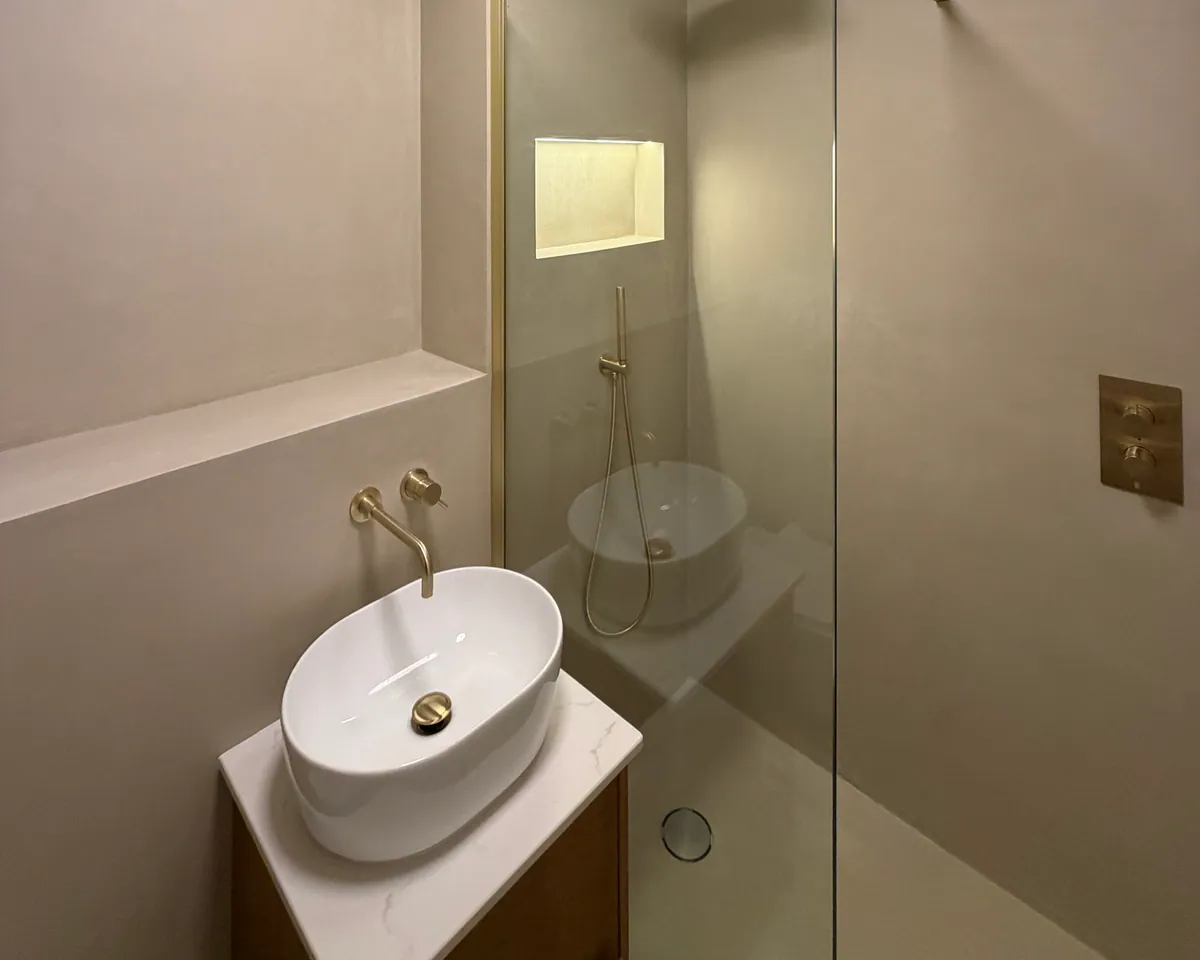 Vessel basin and brass tap beside a glass shower screen and a lit wall niche