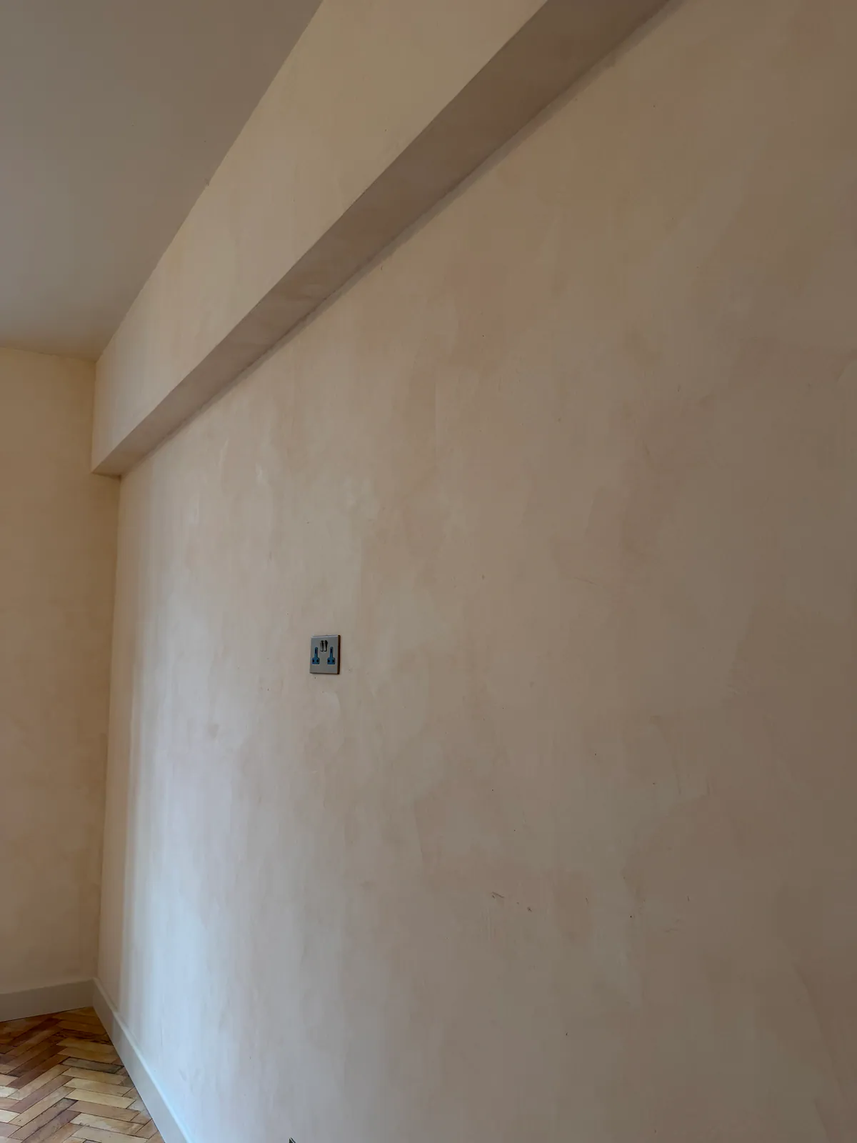 Plaster wall with soft trowel marks, a boxed bulkhead above and a steel socket