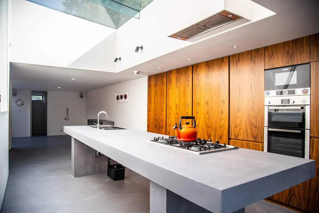 Grey kitchen island with a gas hob in front of timber cabinet doors and a built-in oven
