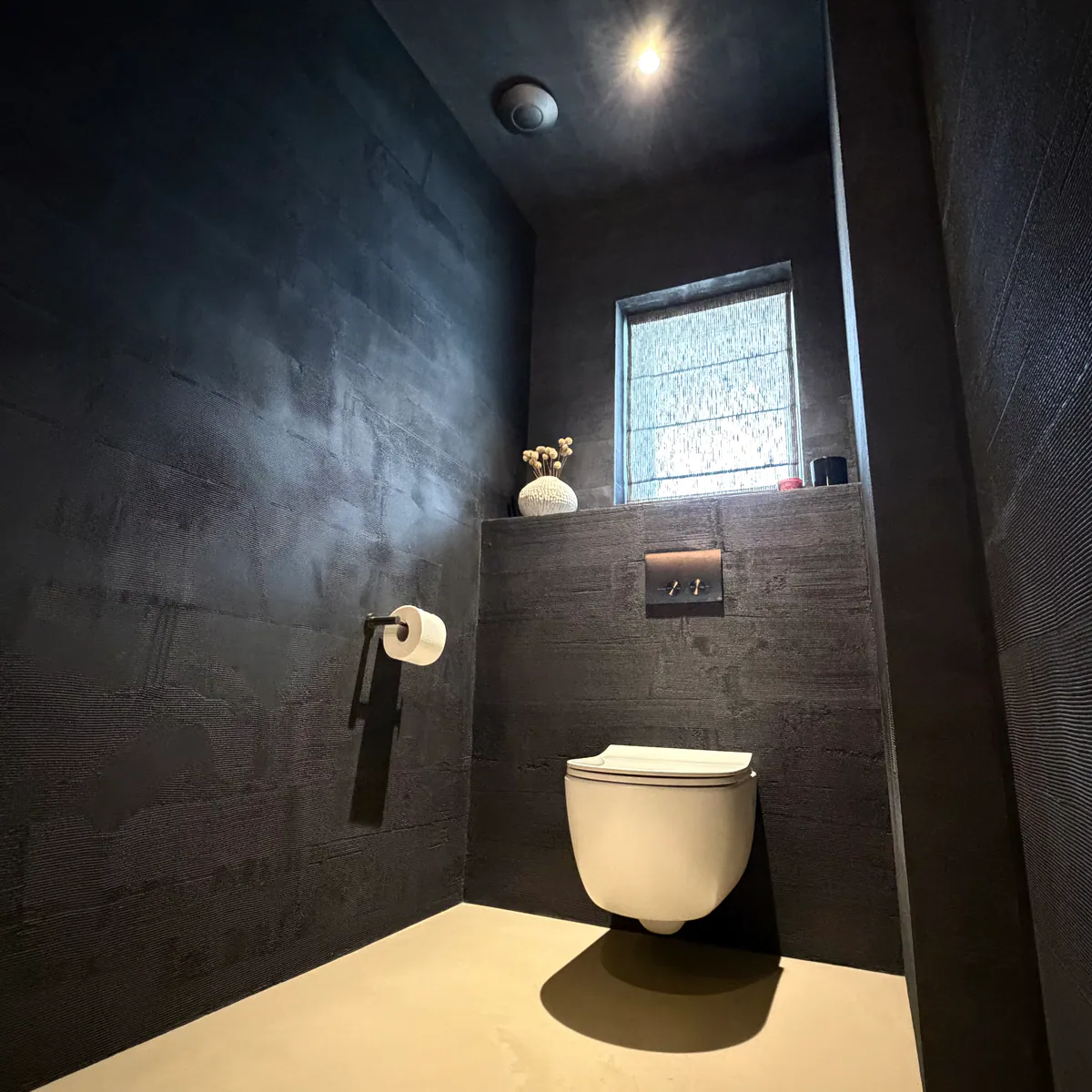 Cloakroom with dark, horizontally textured walls, a wall-hung toilet and a sand-coloured floor