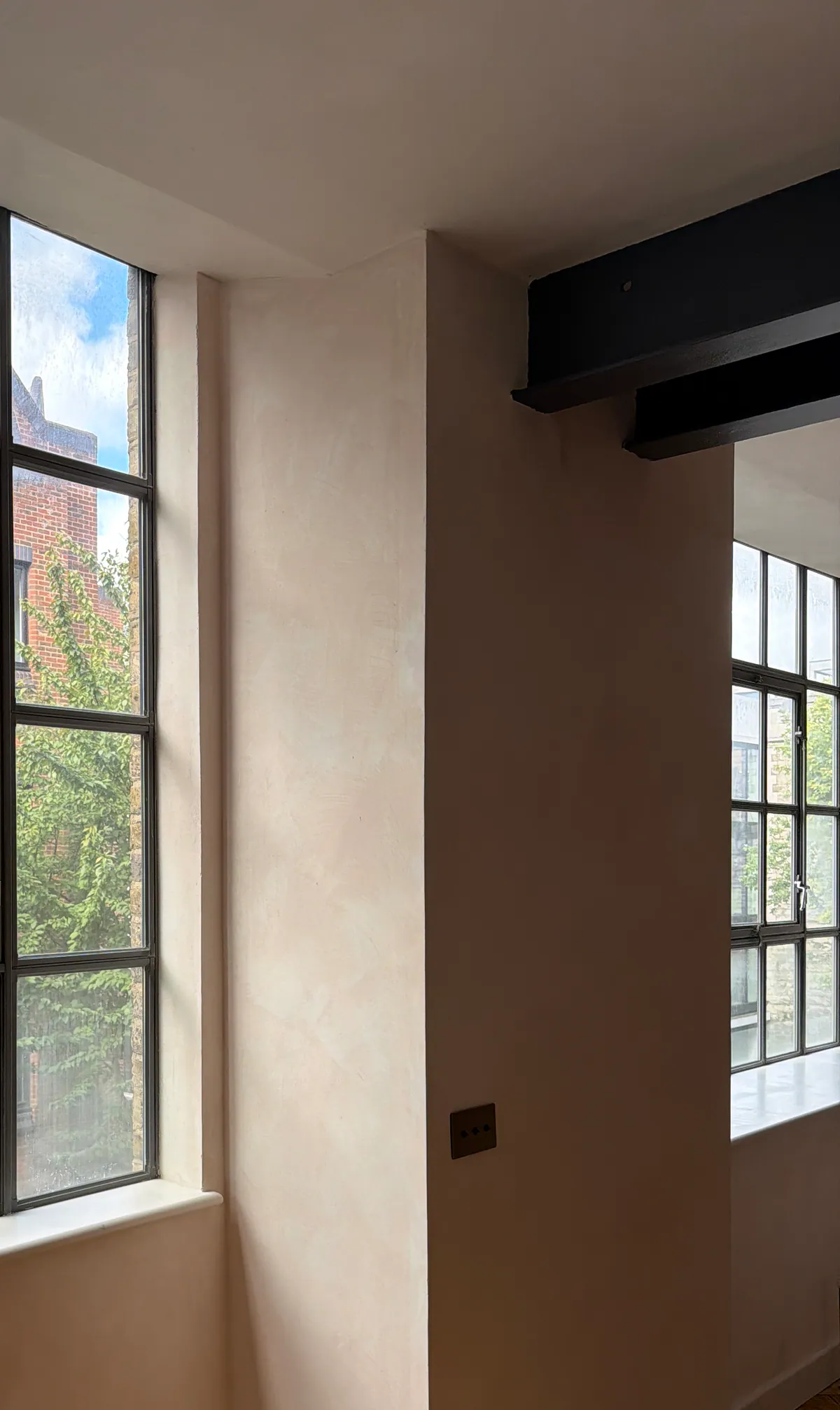 Plaster pier between two steel-framed windows in daylight, with a dark steel beam above